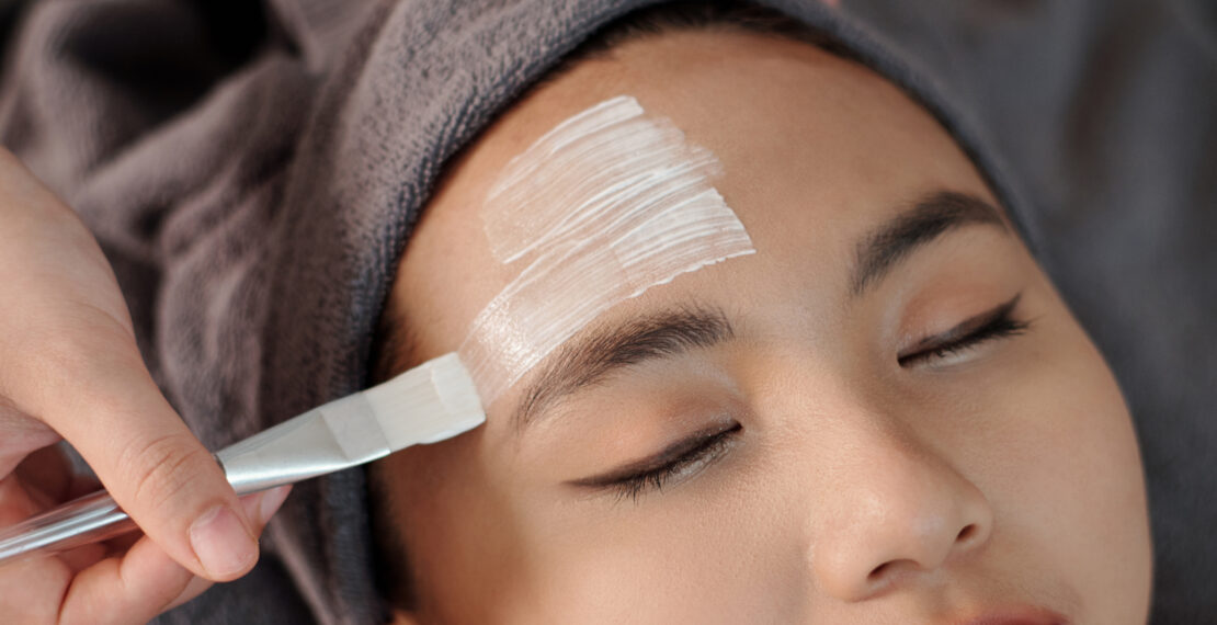 Esthetician applying moisturizing mask on face of young woman